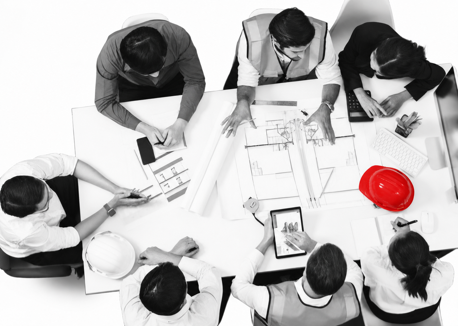 Top-down view of a diverse team collaborating on architectural blueprints around a table; a red hard hat stands out of the grayscale scene.